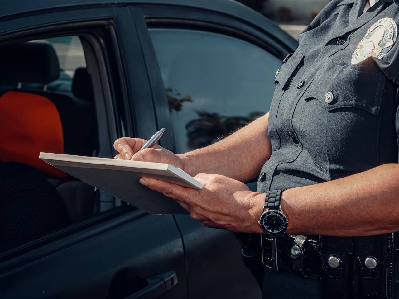 Close-up of a police officer writing a ticket by a car window. Law enforcement scene.